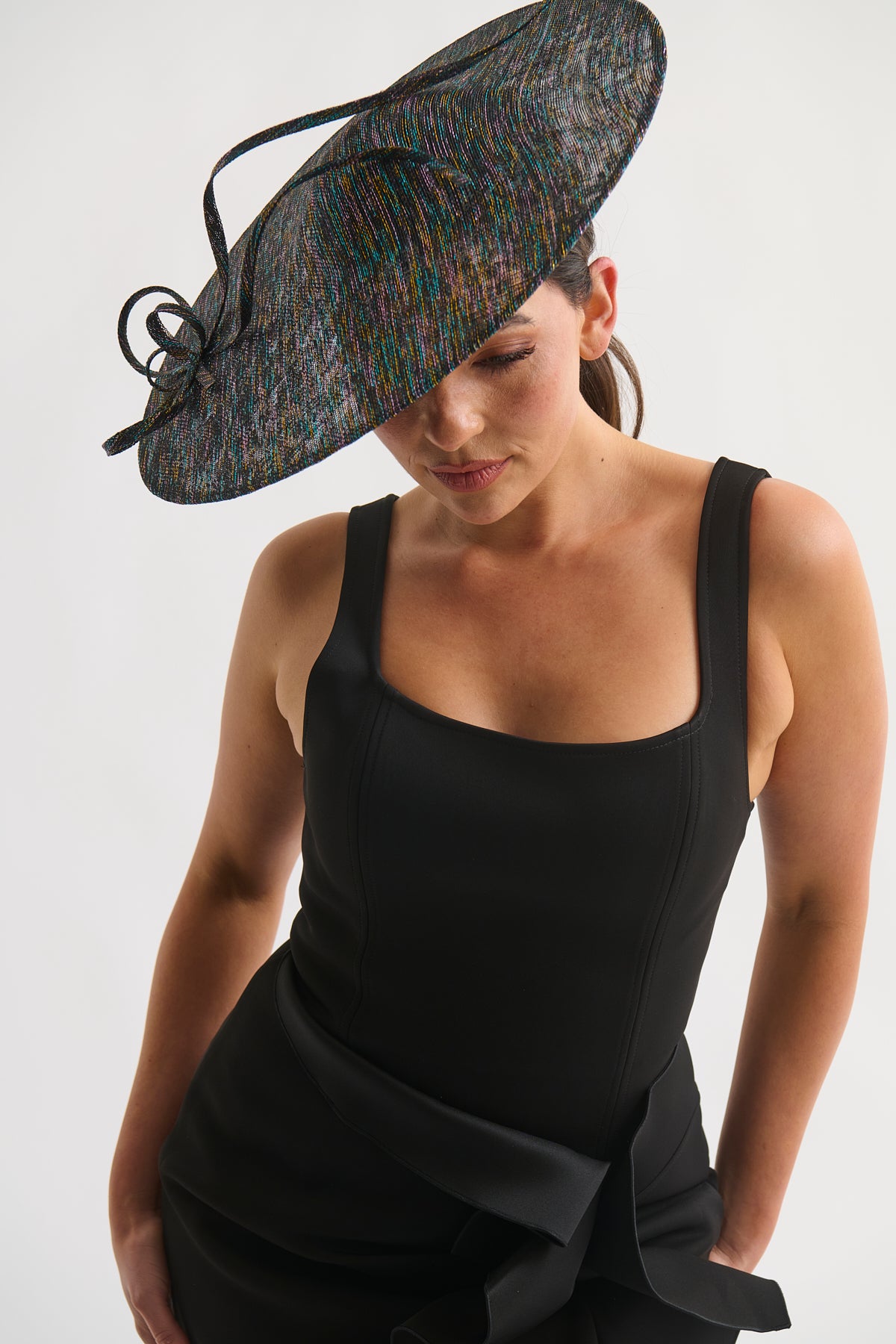 Woman wearing a large decorative hat and a black dress on a white background