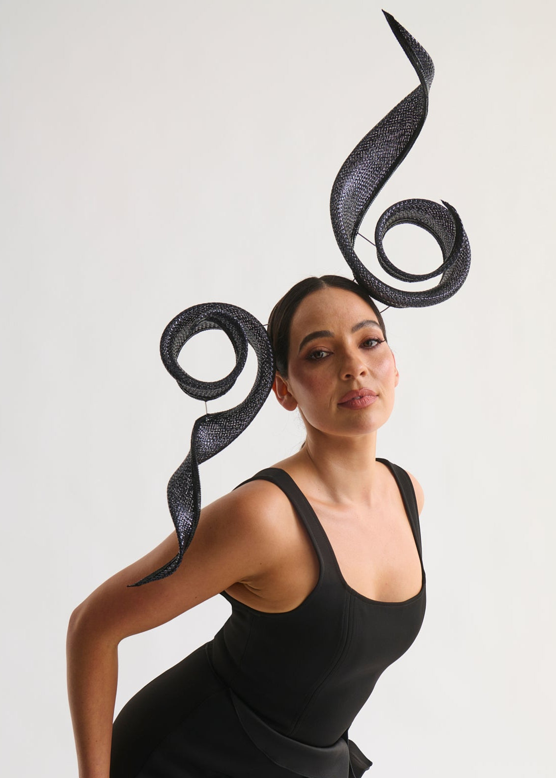 Woman wearing a black dress with a large, decorative headpiece on a white background