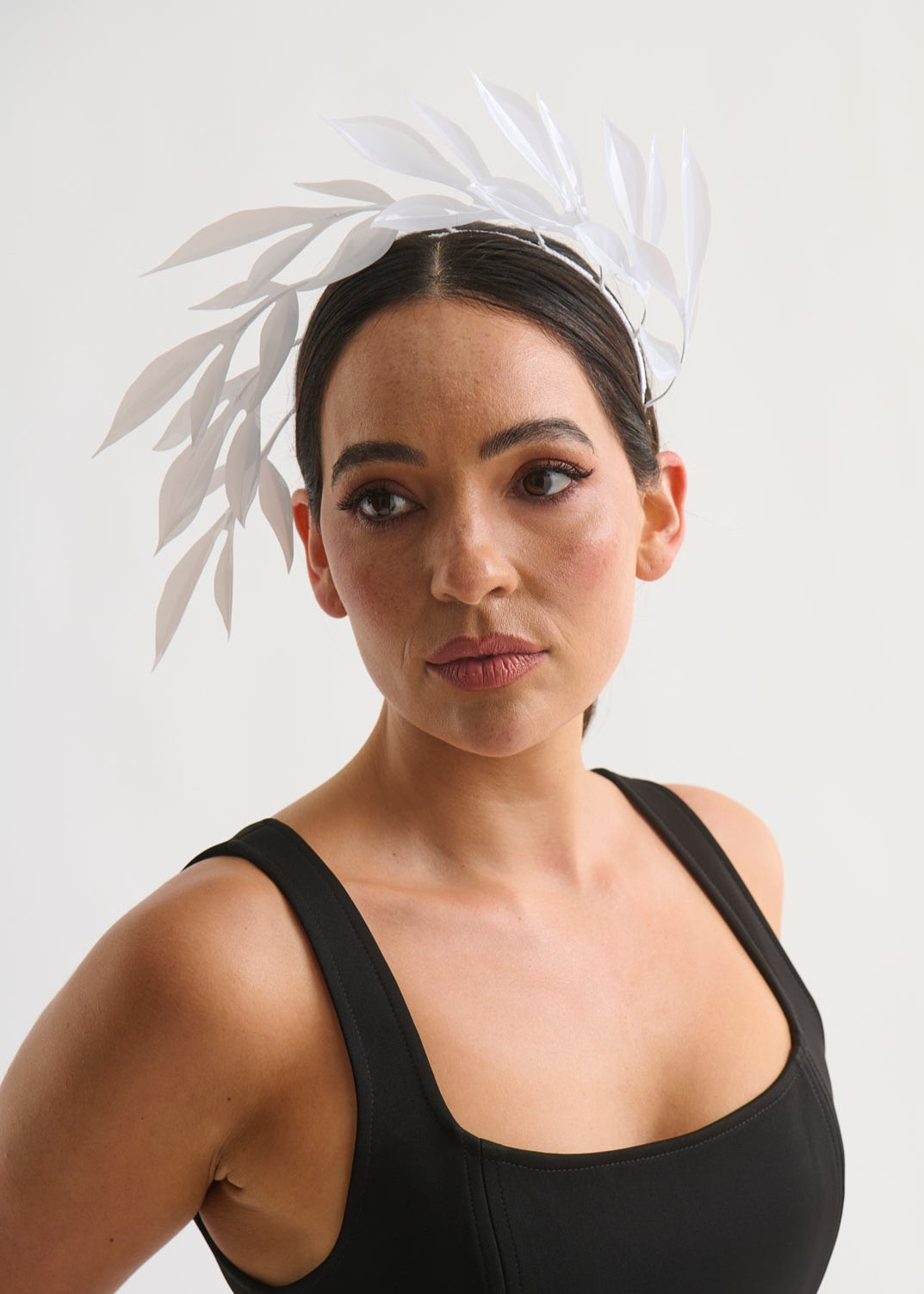 Woman wearing a white leaf headpiece and black dress with a white background