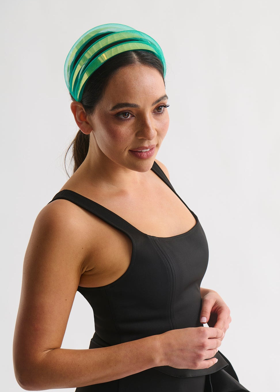 Woman wearing a green headband and black dress against a white background