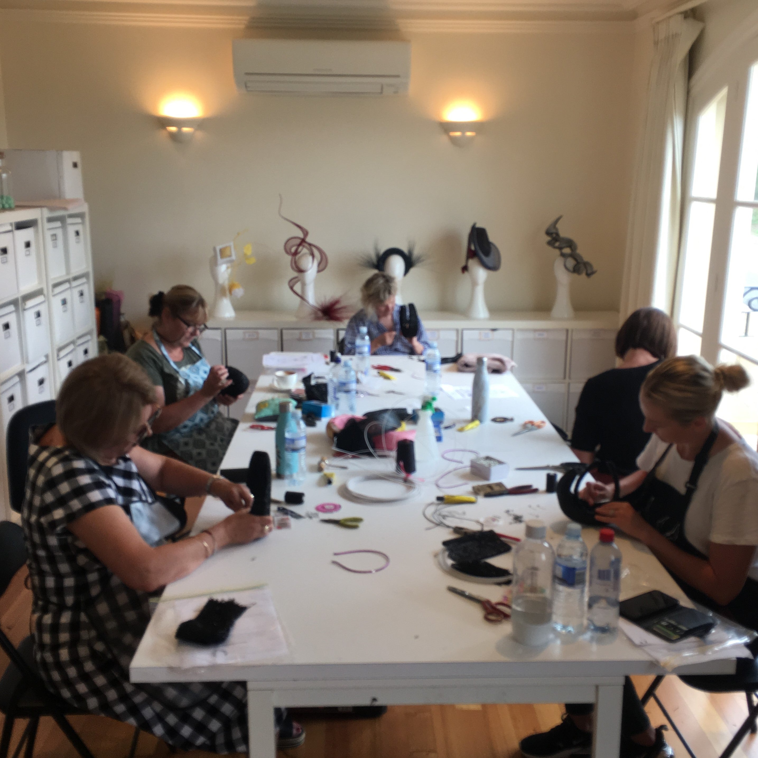 Students working at a white table in a millinery workshop learning how to make hats