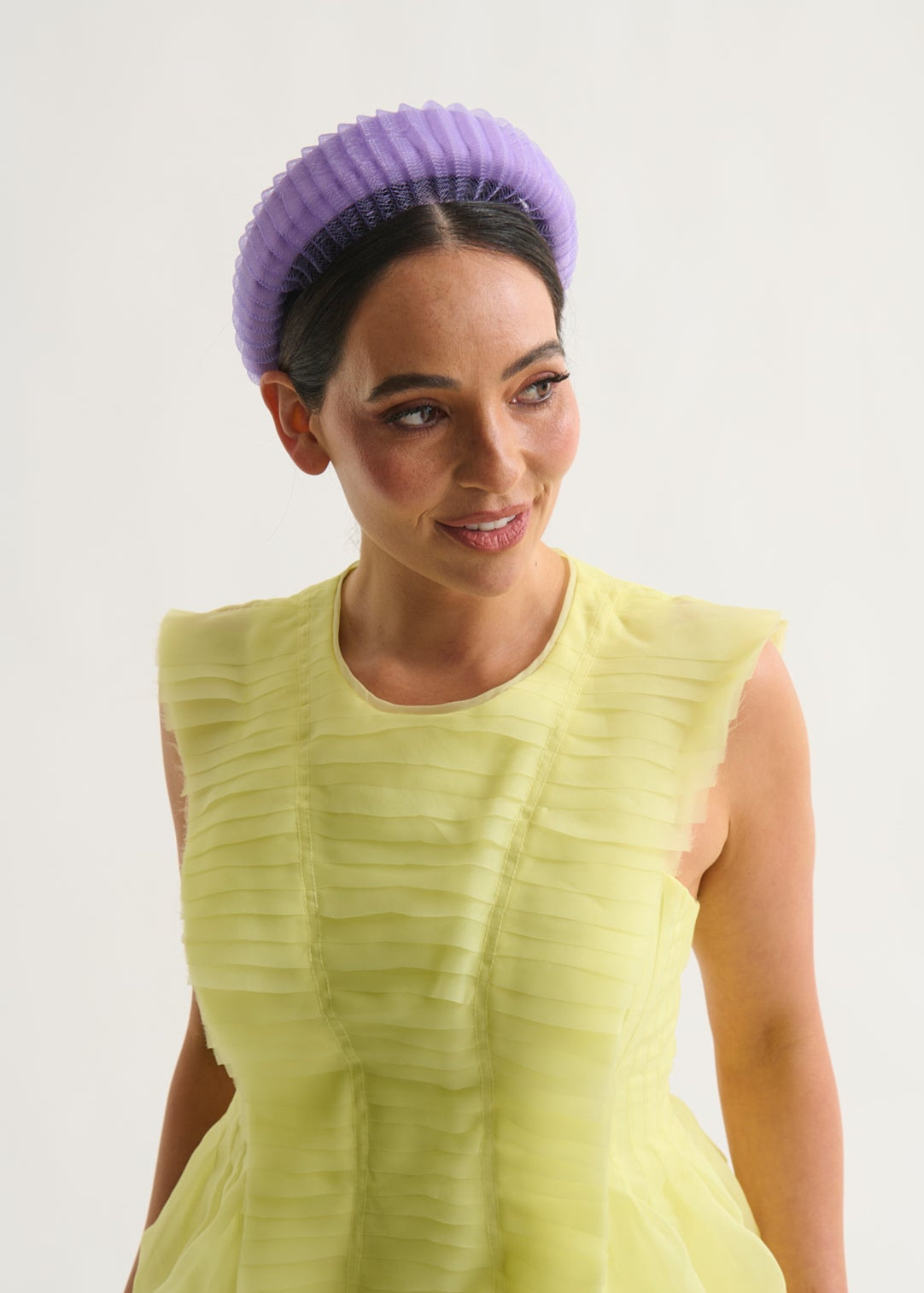 Woman wearing a yellow dress and purple headband against a white background