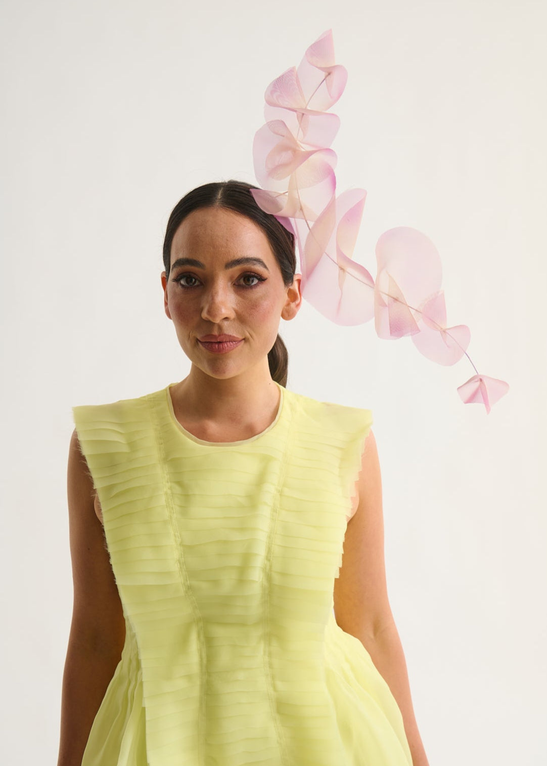 Woman wearing a lilac ruffle headpiece and a yellow dress against a white background