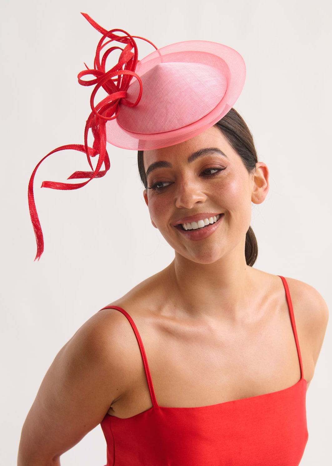 Woman wearing a pink fascinator with red ribbons on a white background