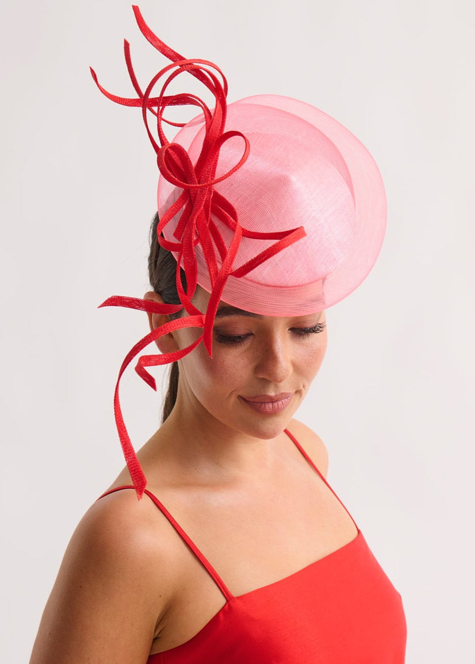 Woman wearing a red dress and pink fascinator with red decorations on a white background