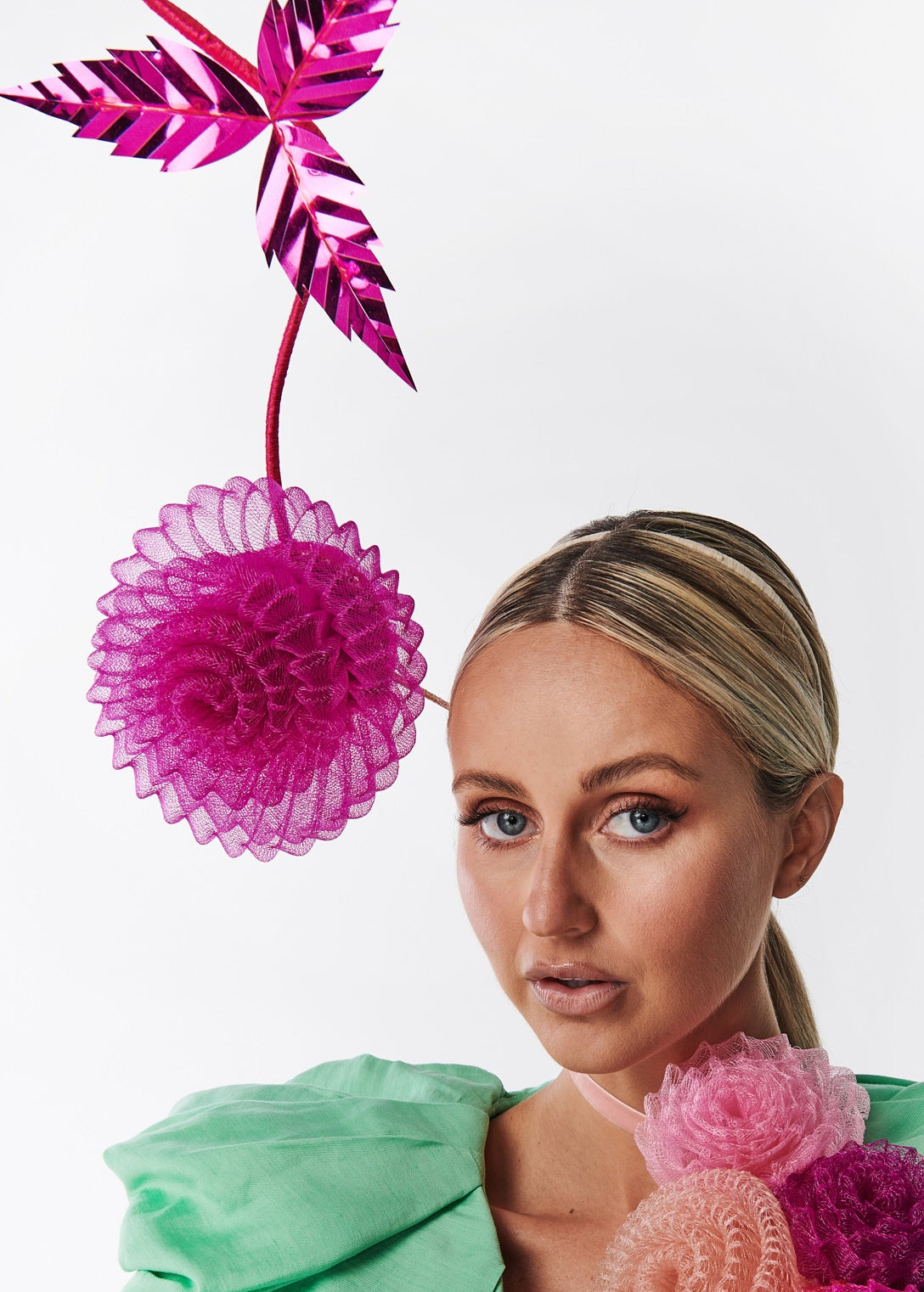 Woman wearing a green outfit with pink floral accessories against a white background