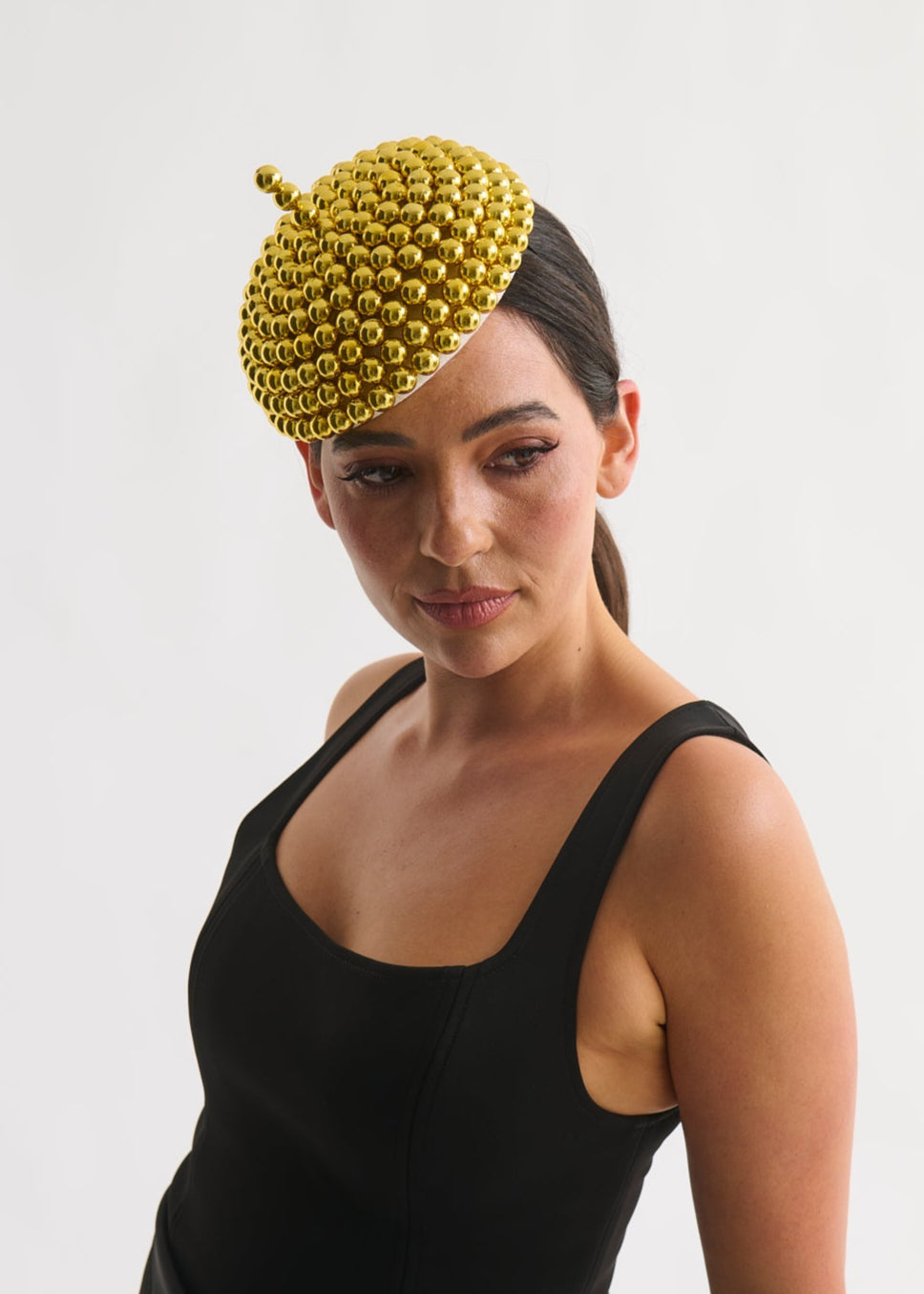 Woman wearing a black dress and gold beaded hat against a white background