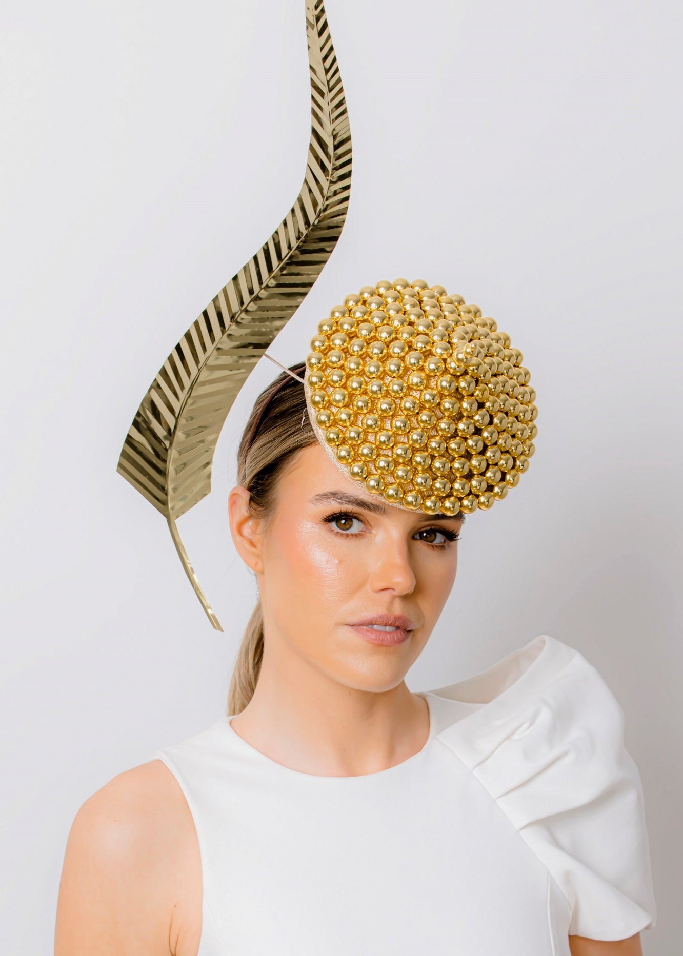 Woman wearing a white dress with a decorative gold headpiece against a plain background