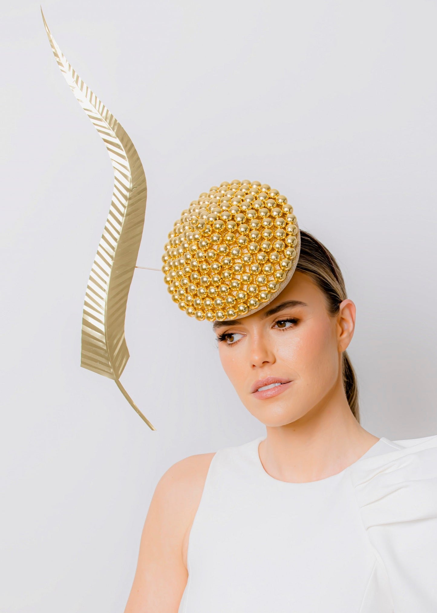 Woman wearing a gold beaded hat with a white dress on a plain background