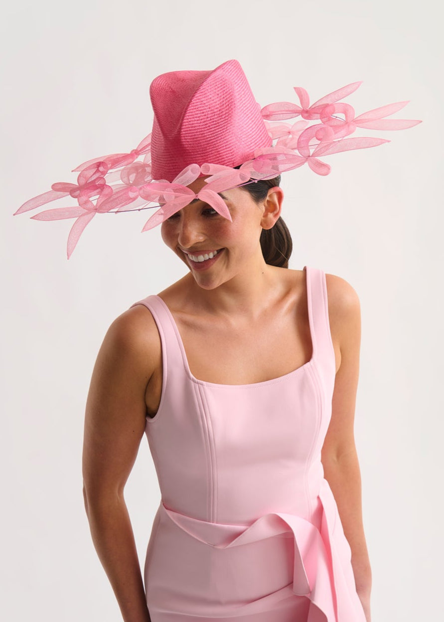 Woman wearing a pink dress and hat with bow details on a white background