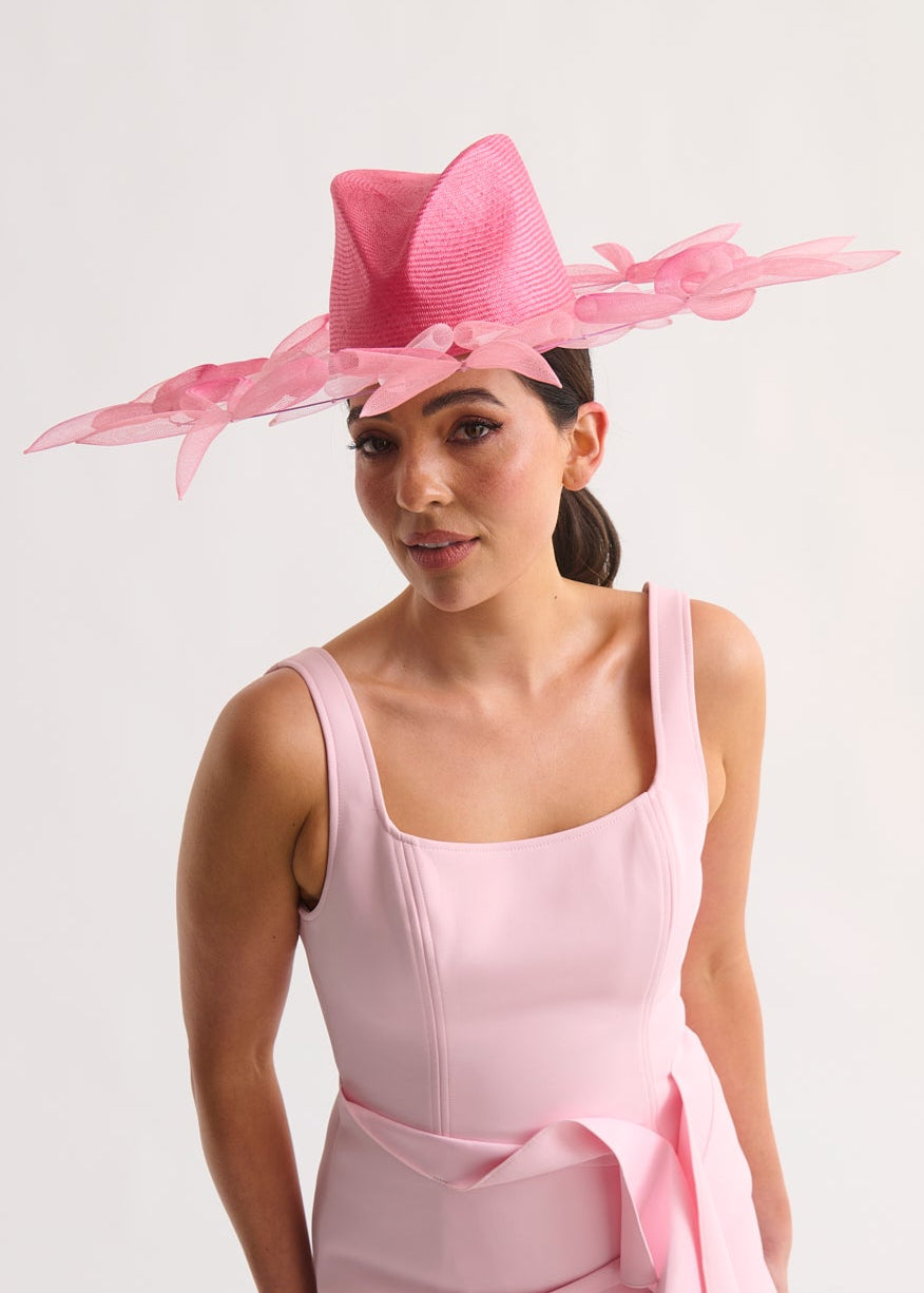 Woman wearing a pink dress and hat against a white background