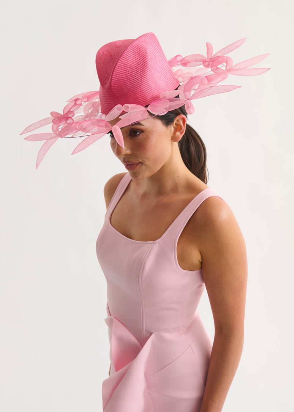 Woman wearing a pink dress and hat with bow details on a white background
