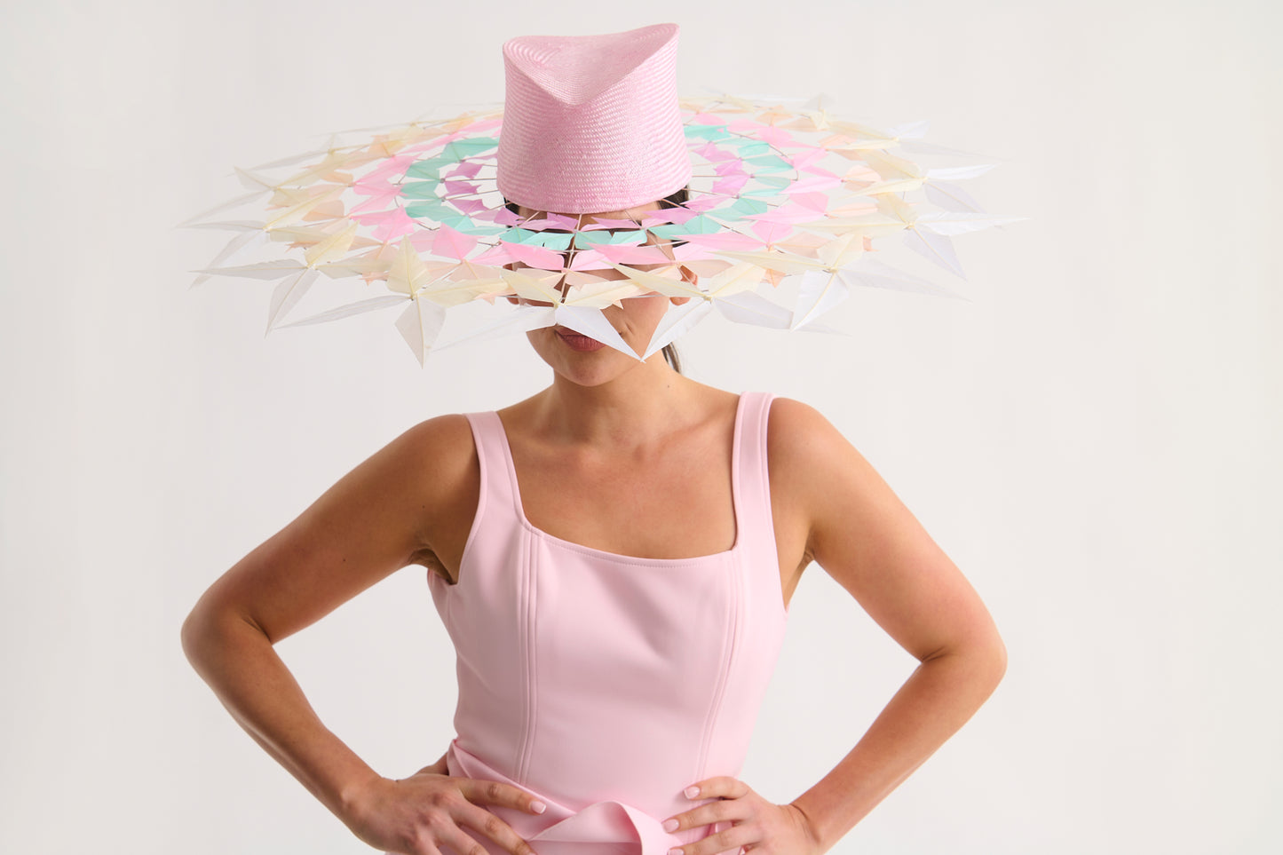 Woman wearing a wide feather brim hat and a pink dress against a white background
