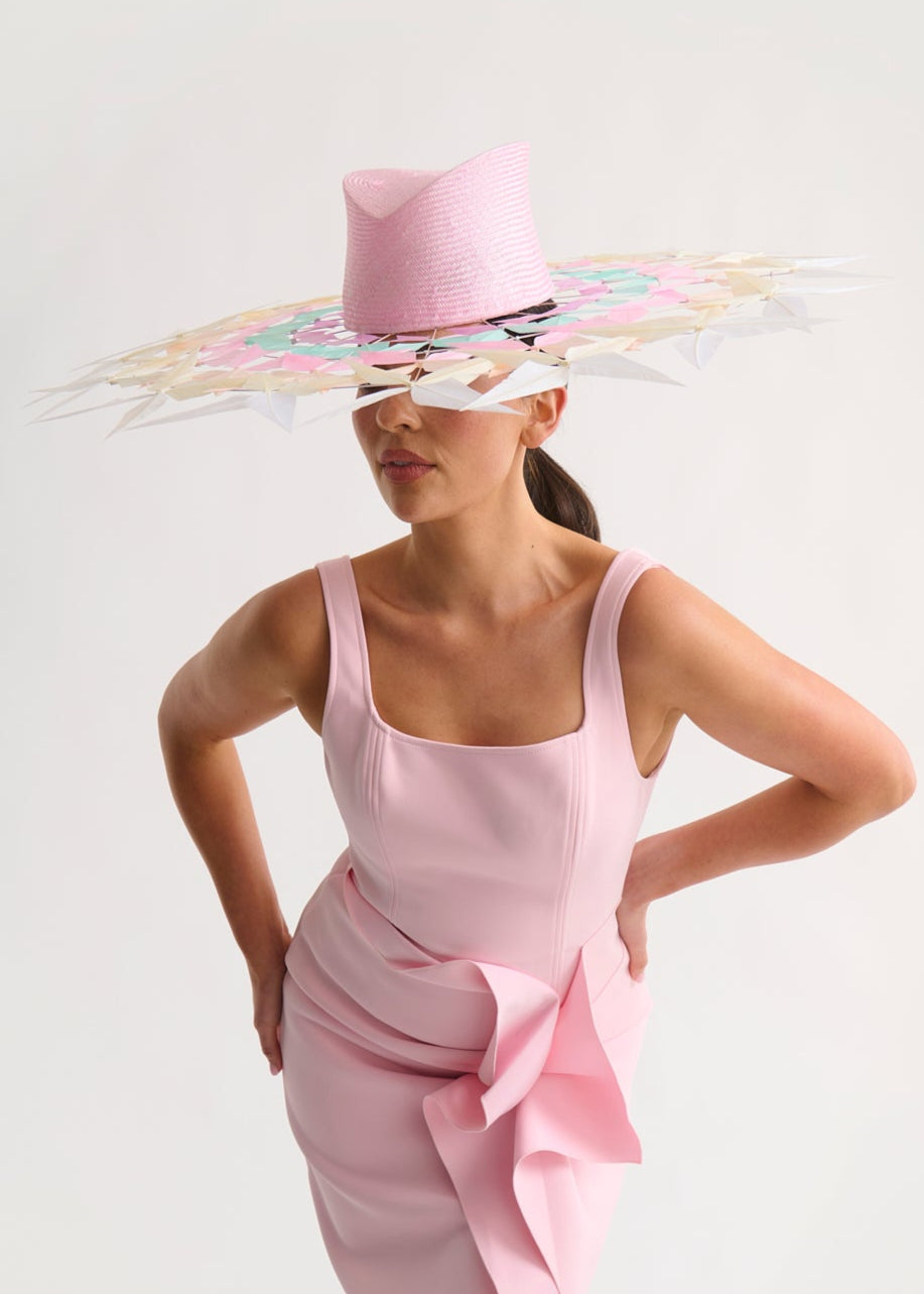 Woman wearing a wide feather brim hat and a pink dress against a white background