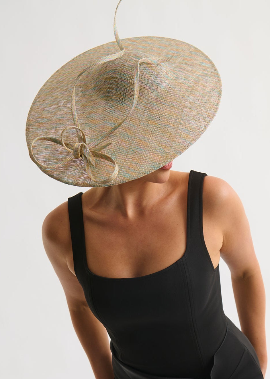 Person wearing a black dress and large decorative hat on a plain background