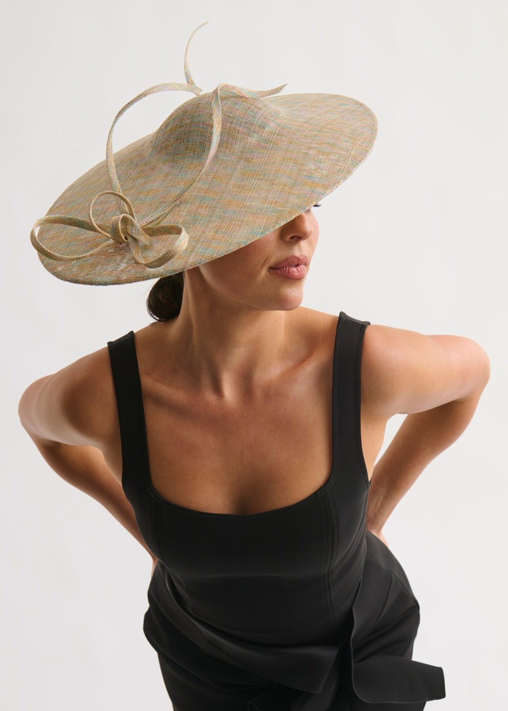 Woman wearing a large decorative hat against a plain background