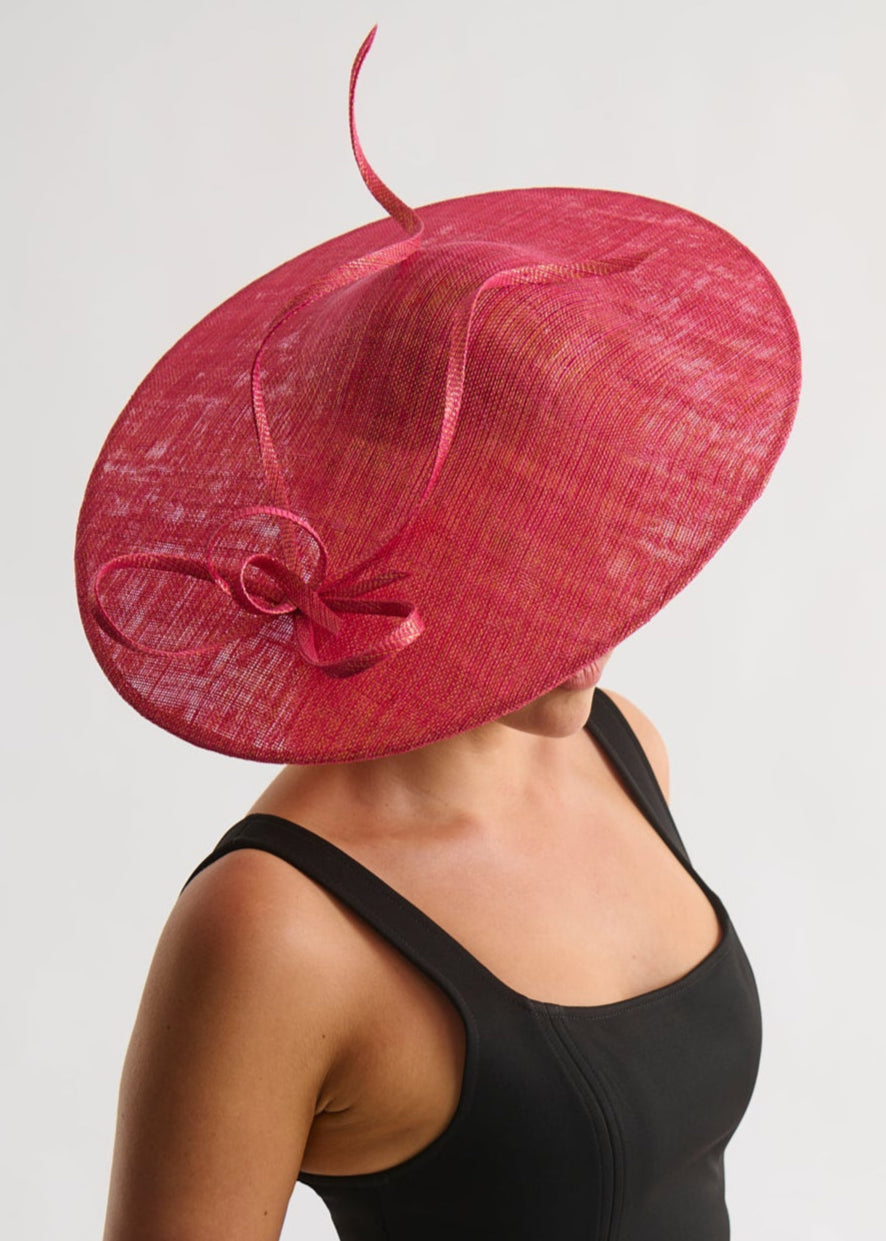 Woman wearing a large pink hat with a bow on a plain background