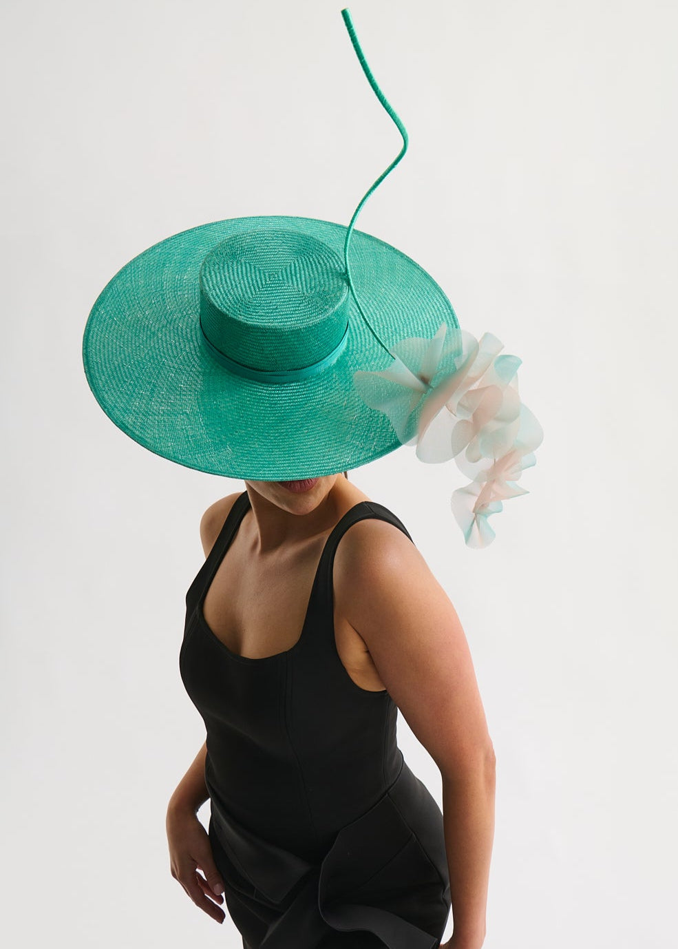 Woman wearing a wide brim hat with ruffle trim and a black dress against a white background
