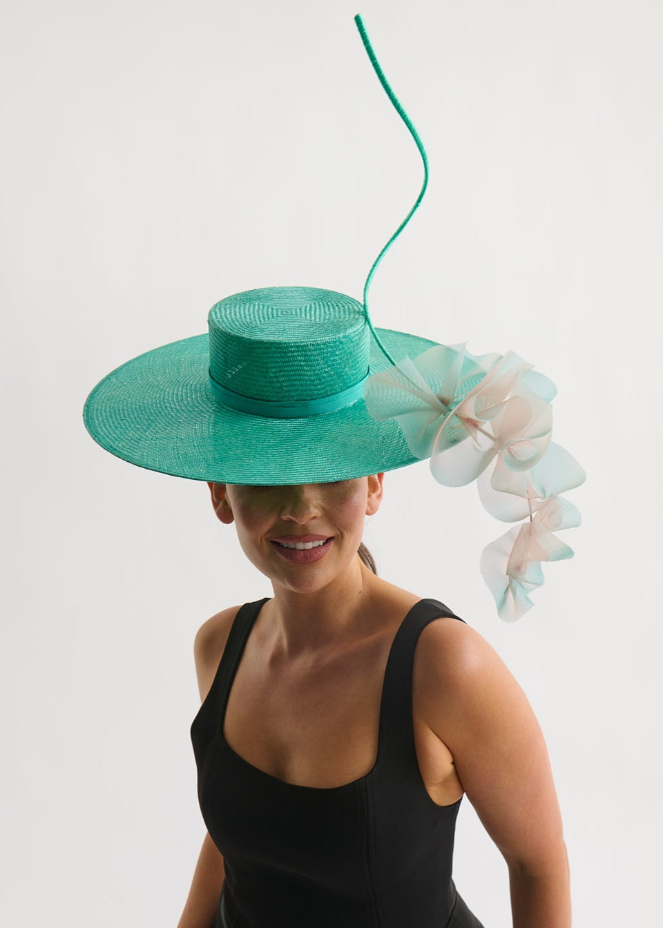 Woman wearing a wide brim hat with ruffle trim and a black dress against a white background