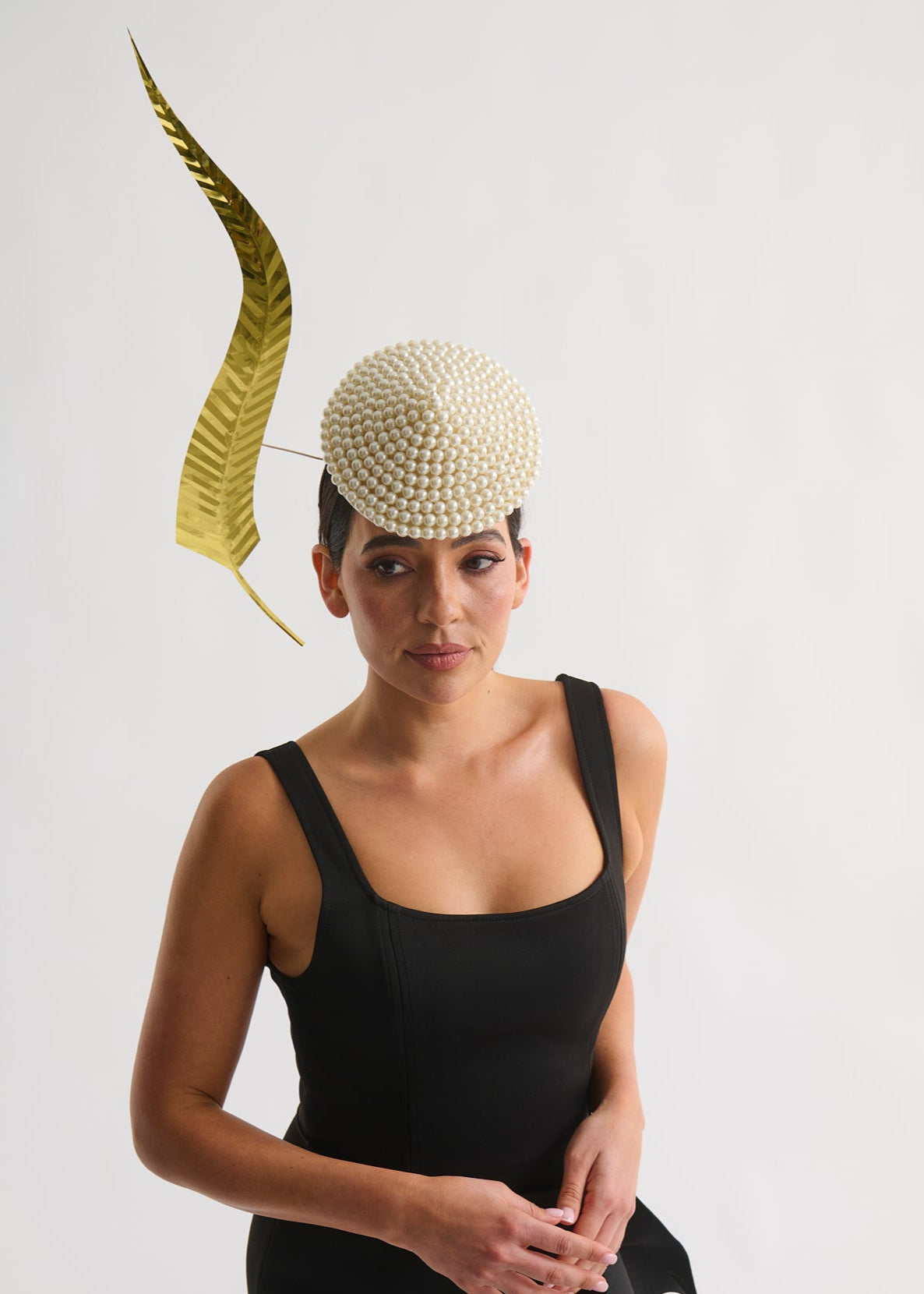 Woman wearing a beaded hat with a long metallic gold feather trim and a black dress against a white background