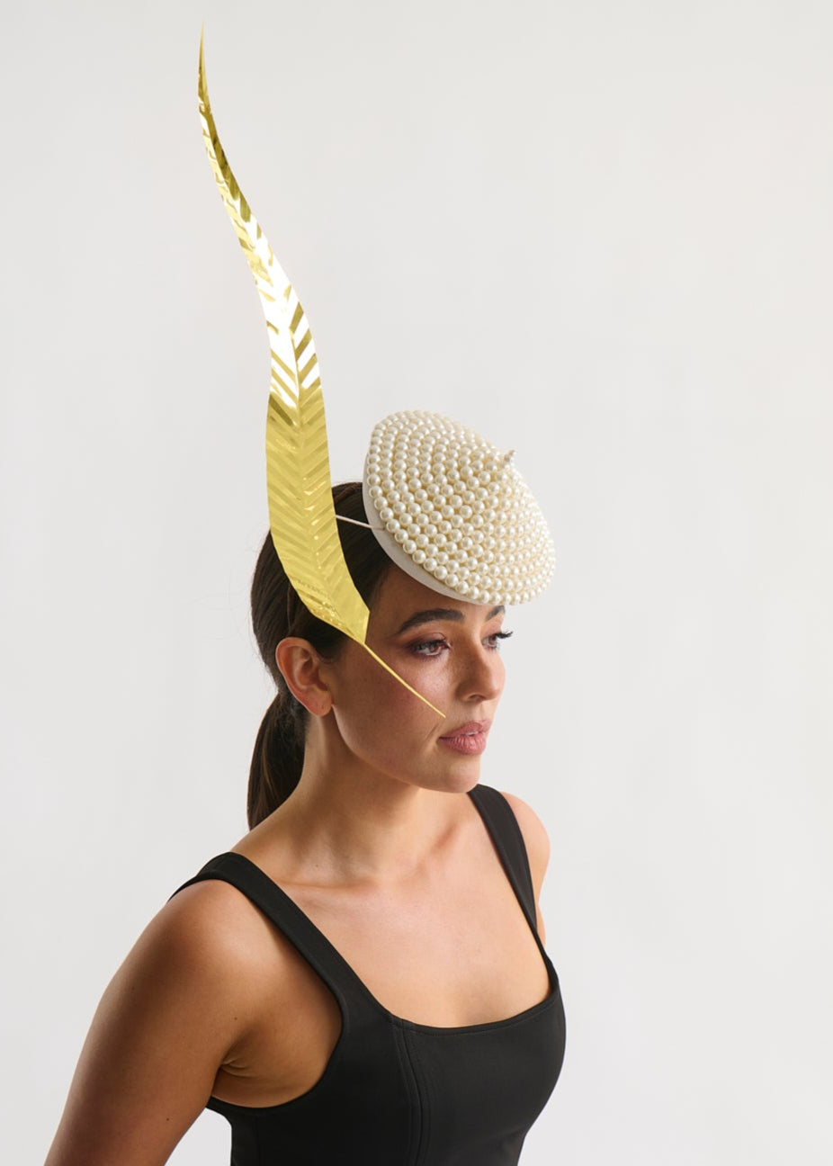 Woman wearing a black dress and decorative headpiece with gold and pearl elements on a light gray background