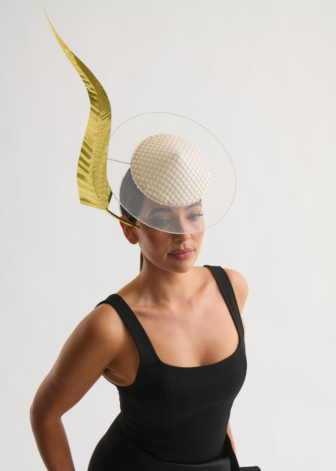 Woman wearing a black dress and a decorative headpiece with a gold feather against a white background