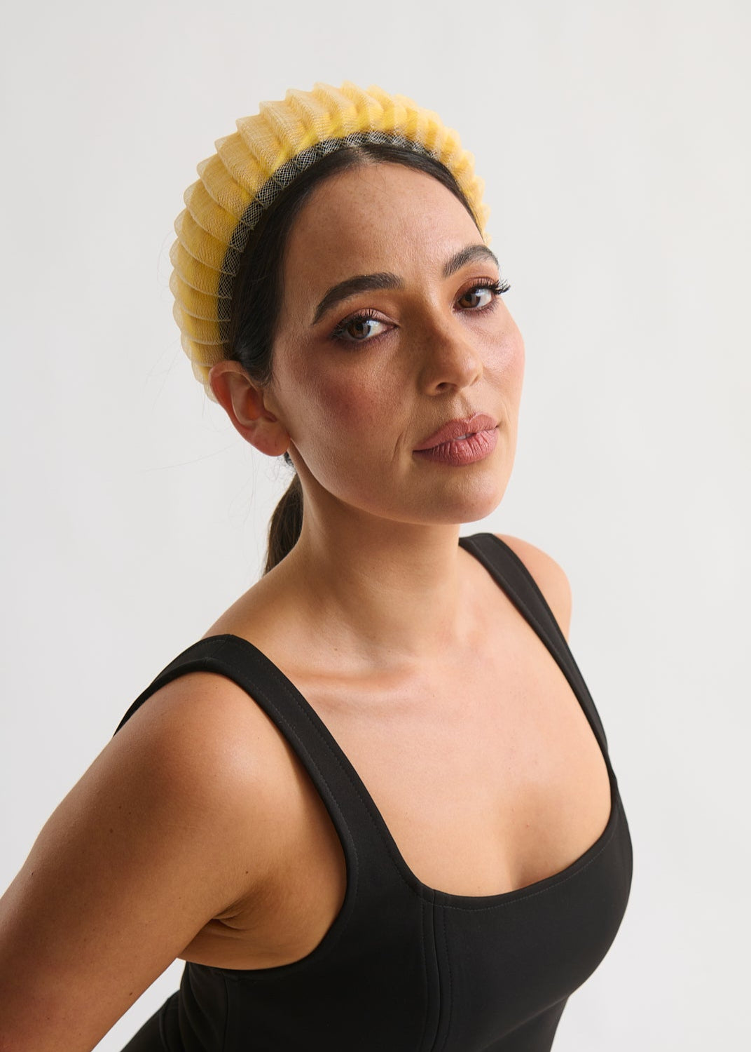 Woman wearing a black dress and yellow headband against a white background