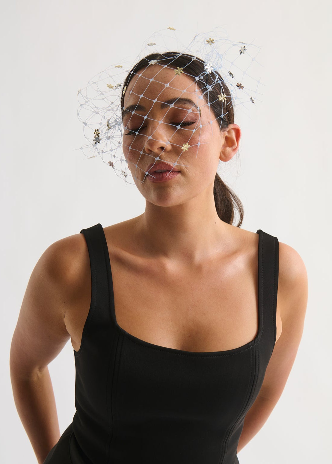 woman wearing a veil with flower sequins and a black dress against a white background