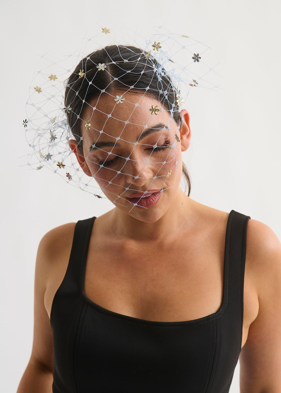 Woman wearing a black dress with a veil headpiece against a light background