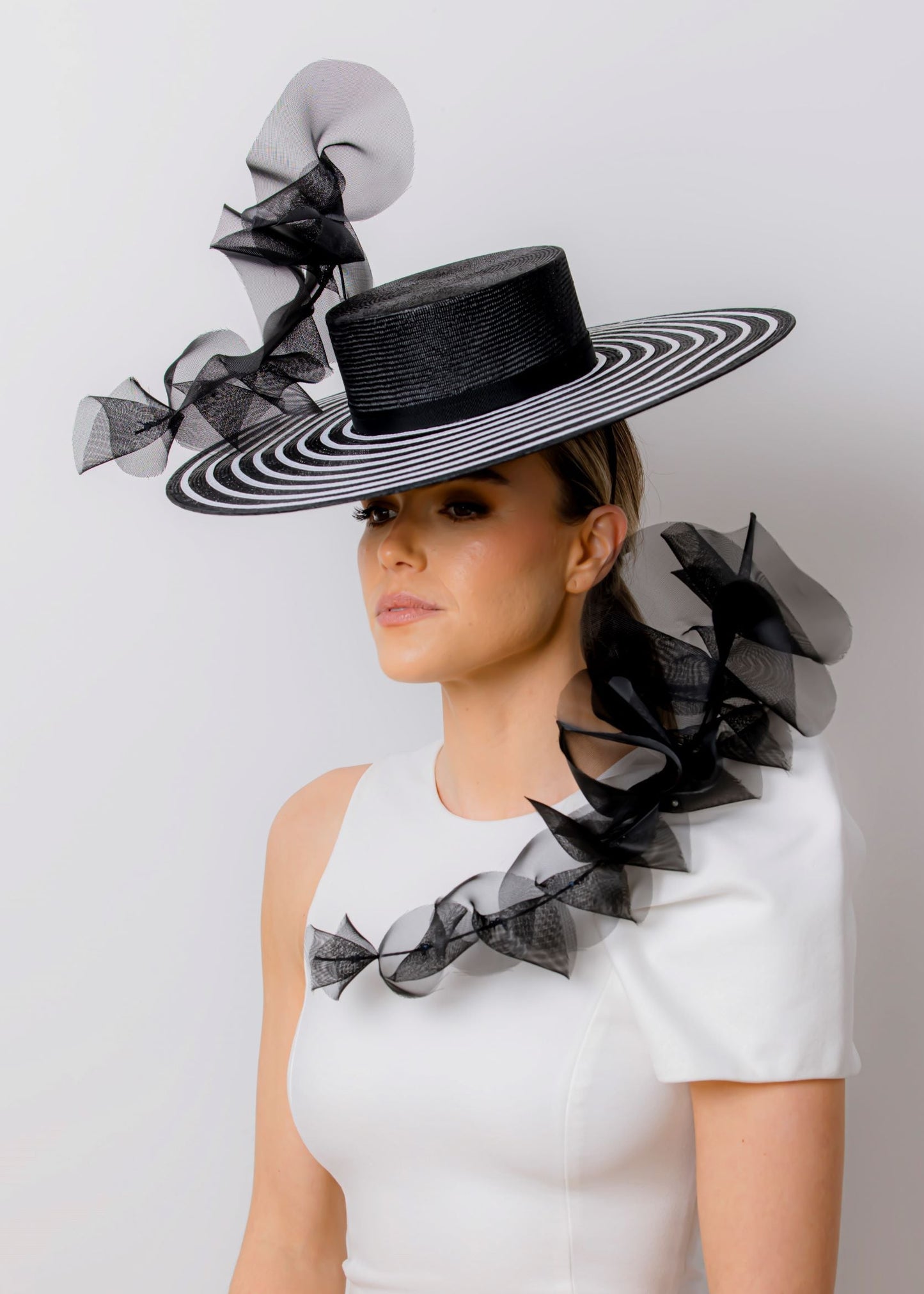 Woman wearing a large black and white striped hat with decorative ribbons on a plain background