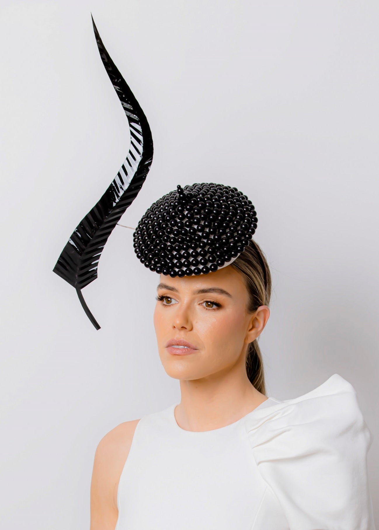 Woman wearing a black beaded hat with a white dress on a light grey background