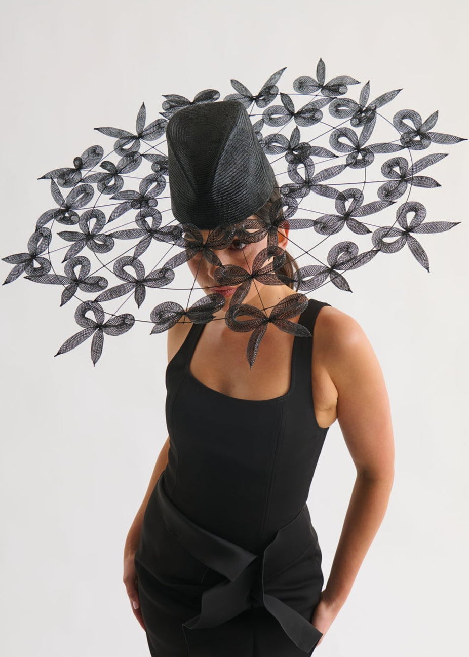 Woman wearing a black dress and hat with bows against a white background
