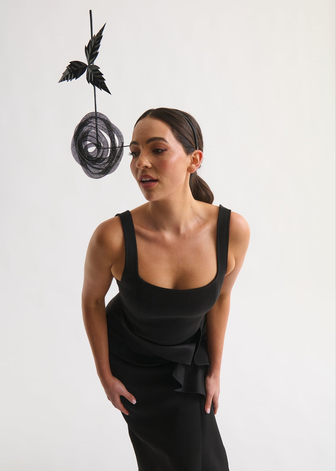 Woman wearing a black dress with a unique headpiece against a white background