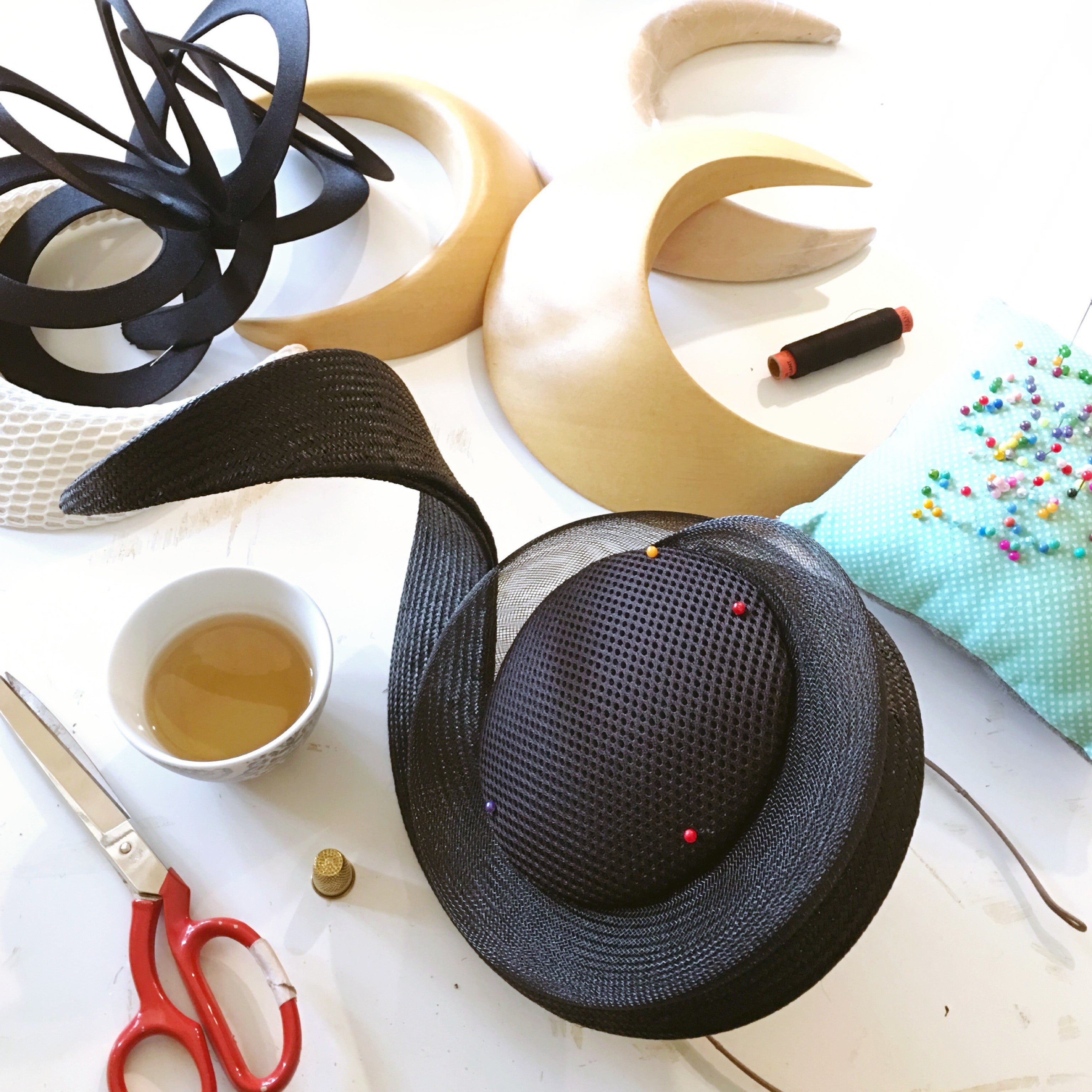 Percher hat millinery tools and hat on a flat lat along with a cup of tea