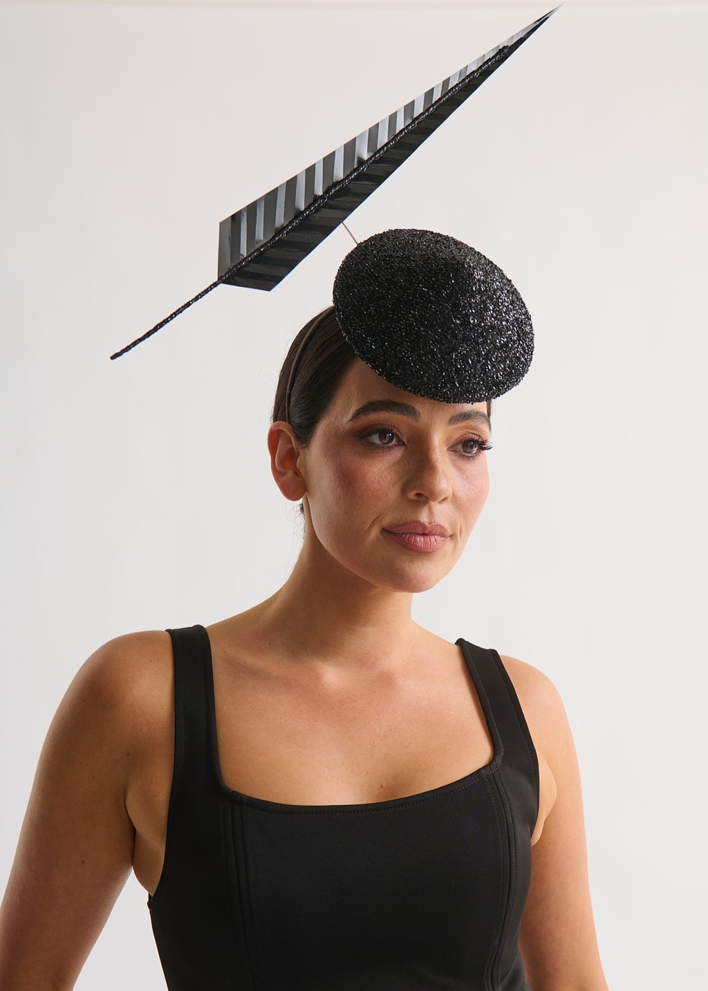 Woman wearing a black dress and decorative hat with a feather against a white background