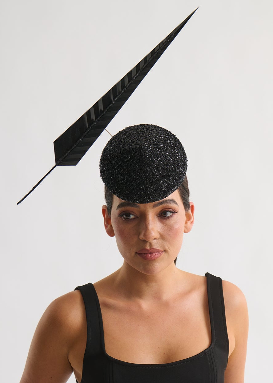 Woman wearing a black dress with a matching black hat against a white background