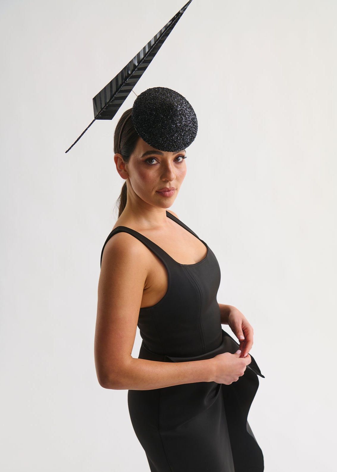 Woman wearing a black dress and hat with a feather against a white background