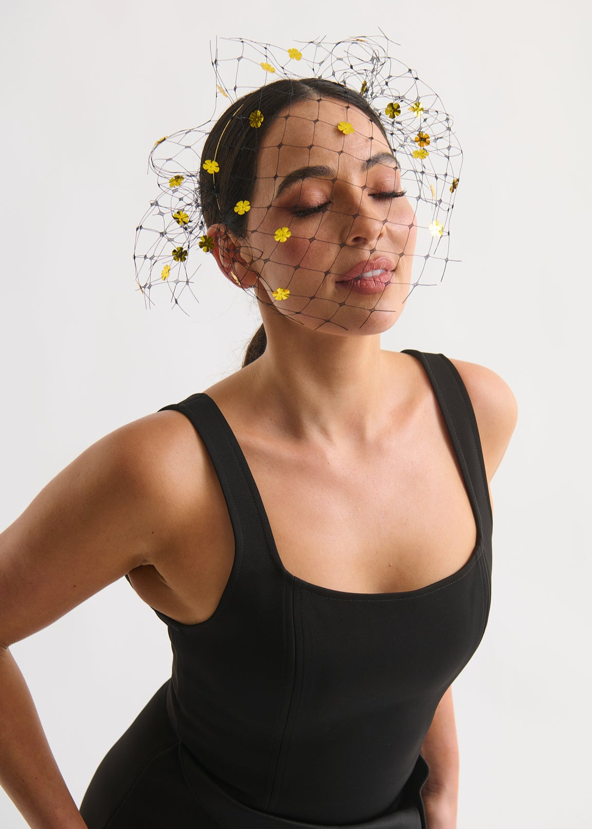 Woman wearing a black sleeveless top with a decorative headpiece against a white background