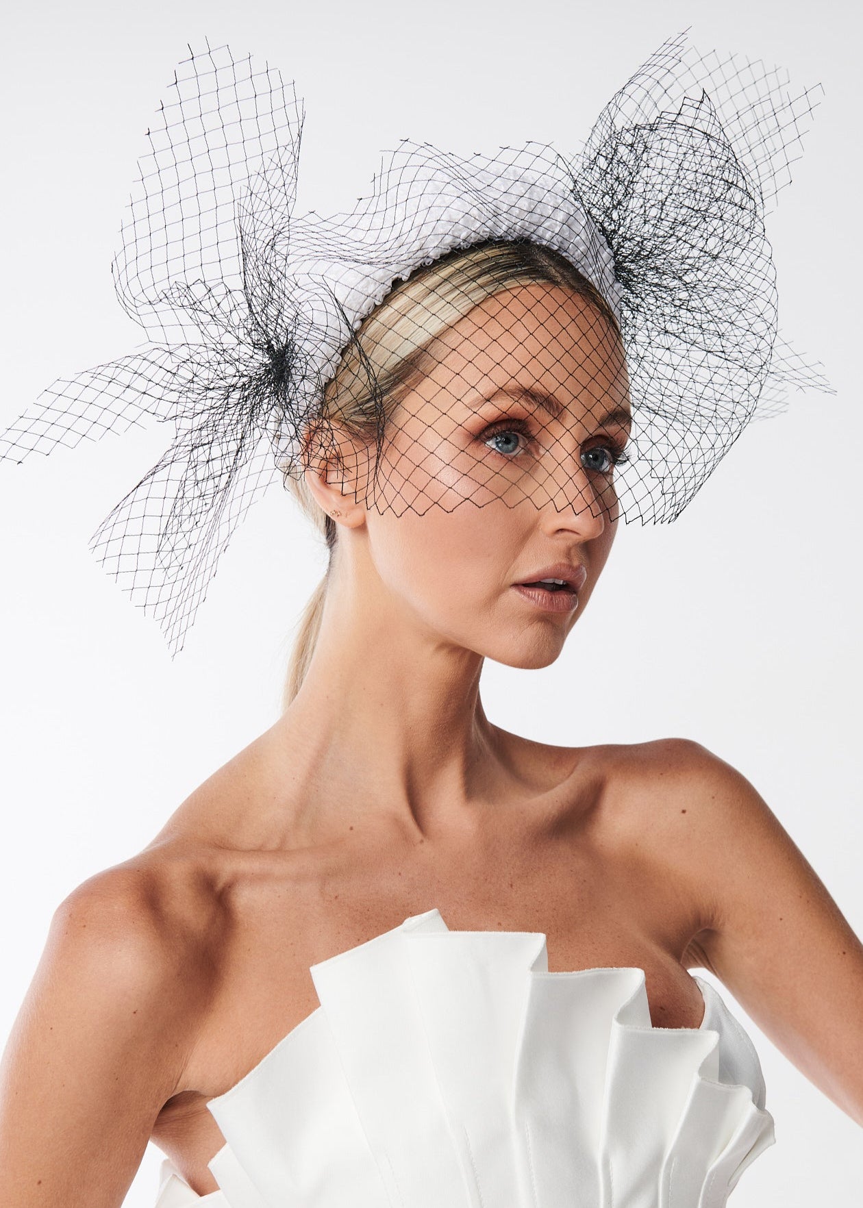 Woman wearing a white strapless dress and a black birdcage veil against a white background