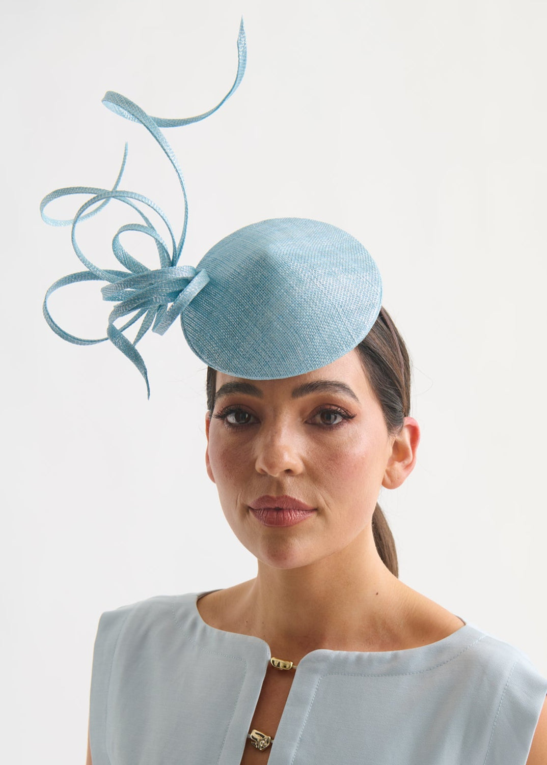 Woman wearing a light blue fascinator with decorative elements on a white background