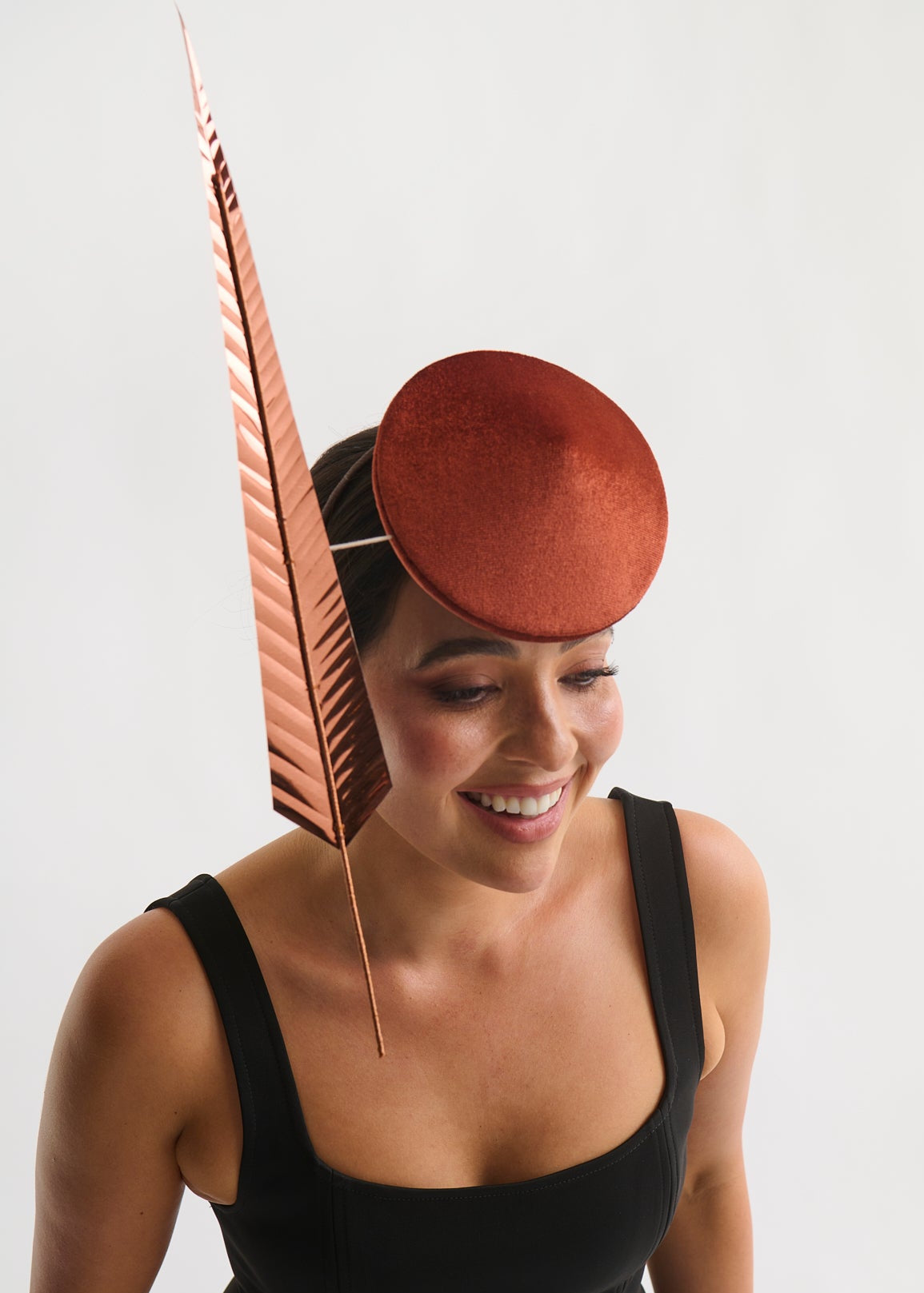 Woman wearing a copper hat with a feather against a white background