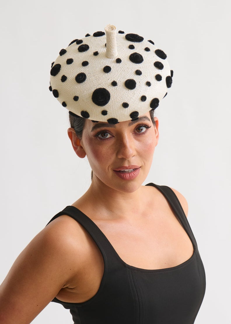 Woman wearing a black dress and polka dot beret hat against a white background