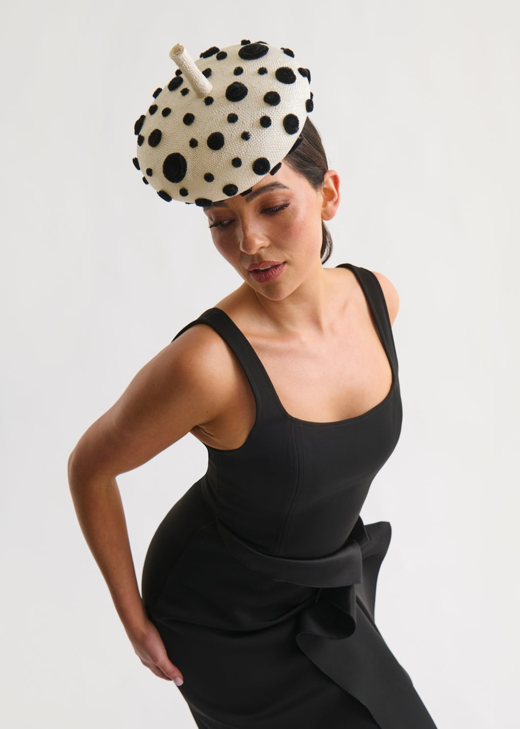Woman wearing a black dress and polka dot hat against a white background
