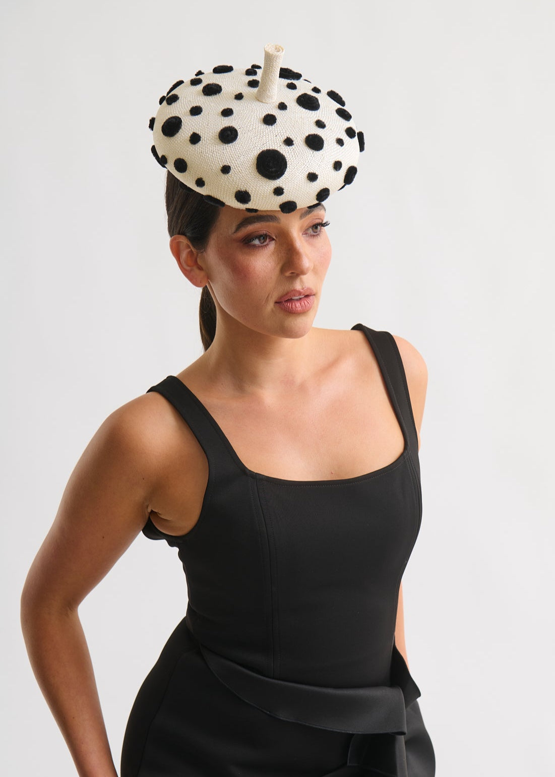 Woman wearing a black dress and polka dot headpiece against a white background