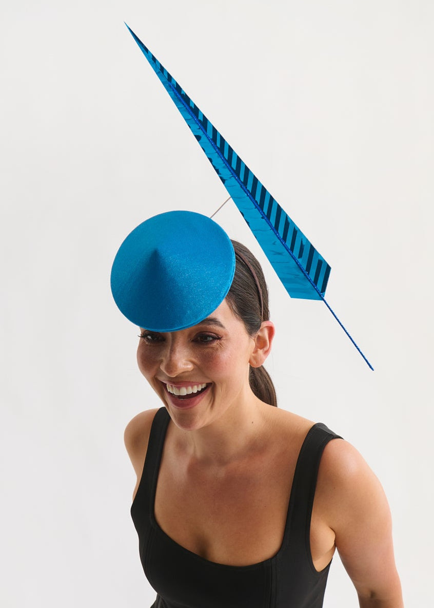 Woman wearing a blue hat with a large blue feather against a white background