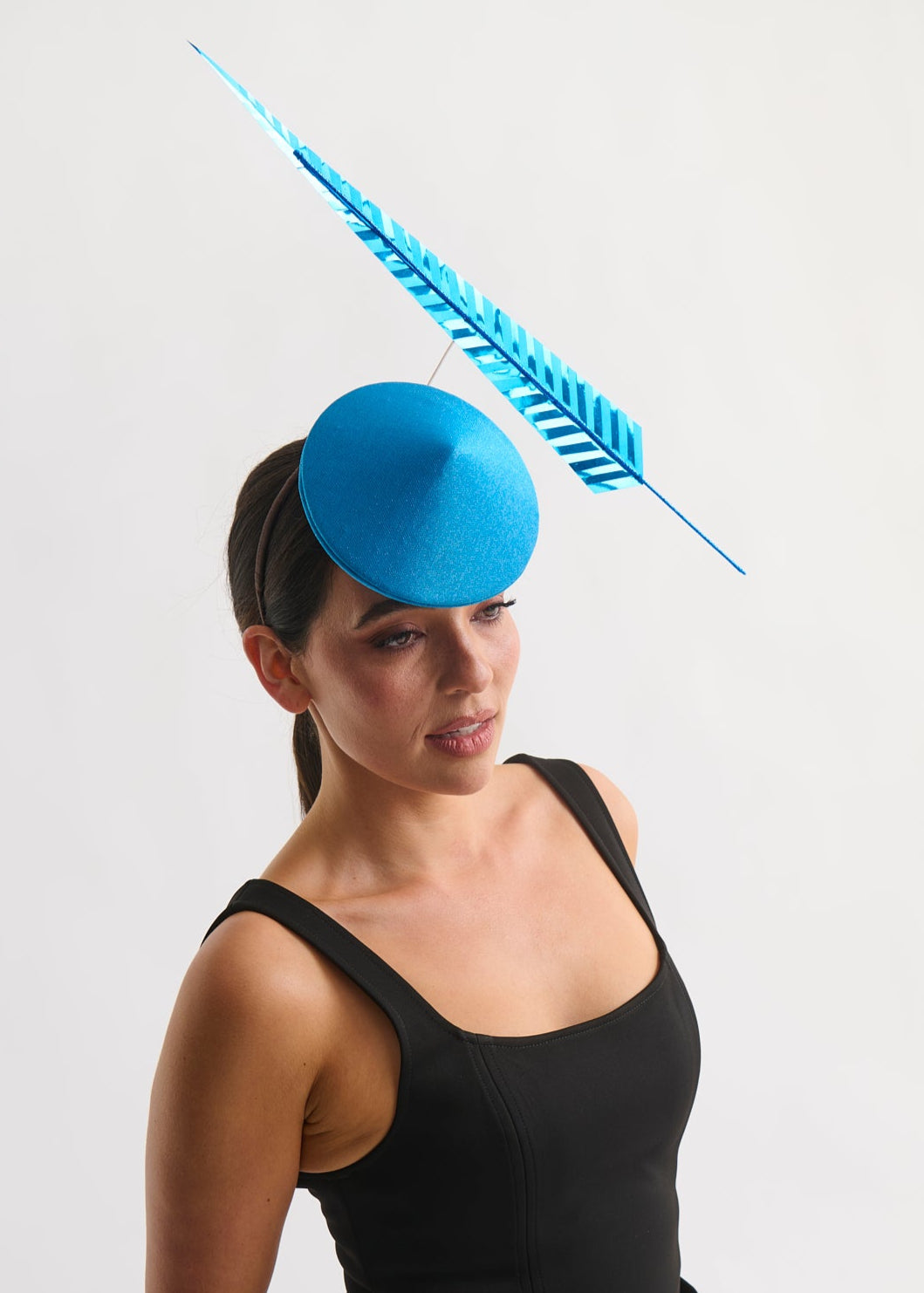 Woman wearing a blue fascinator with a feather on a white background