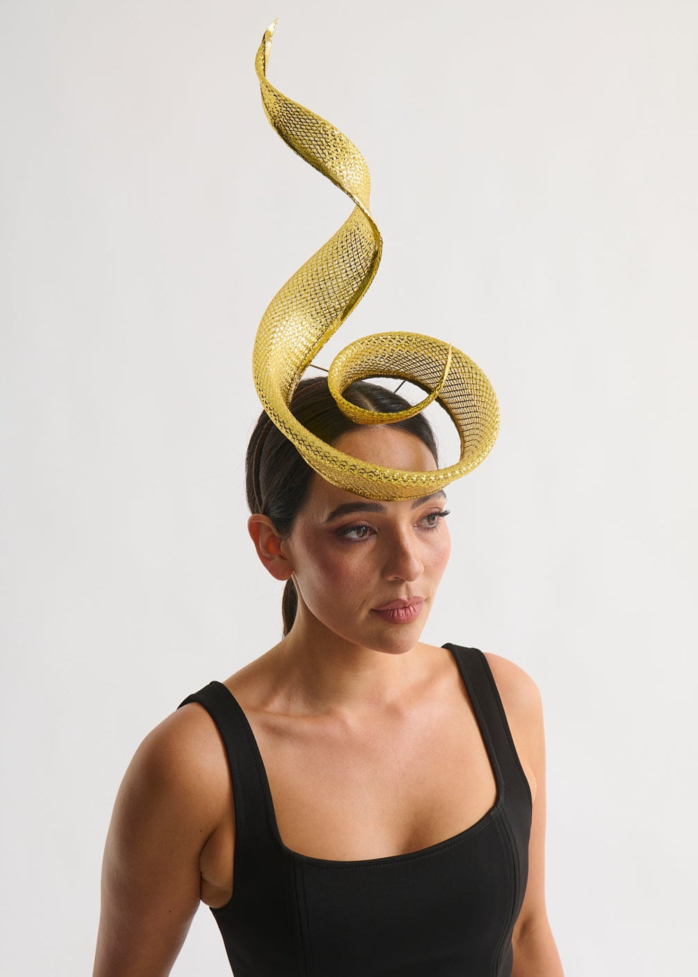 Woman wearing a black dress with a gold swirl headpiece against a white background