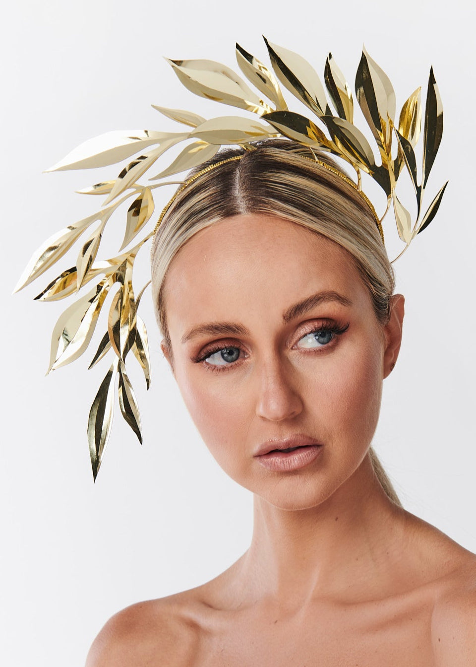 Woman wearing a white strapless dress with a gold leaf headpiece on a white background