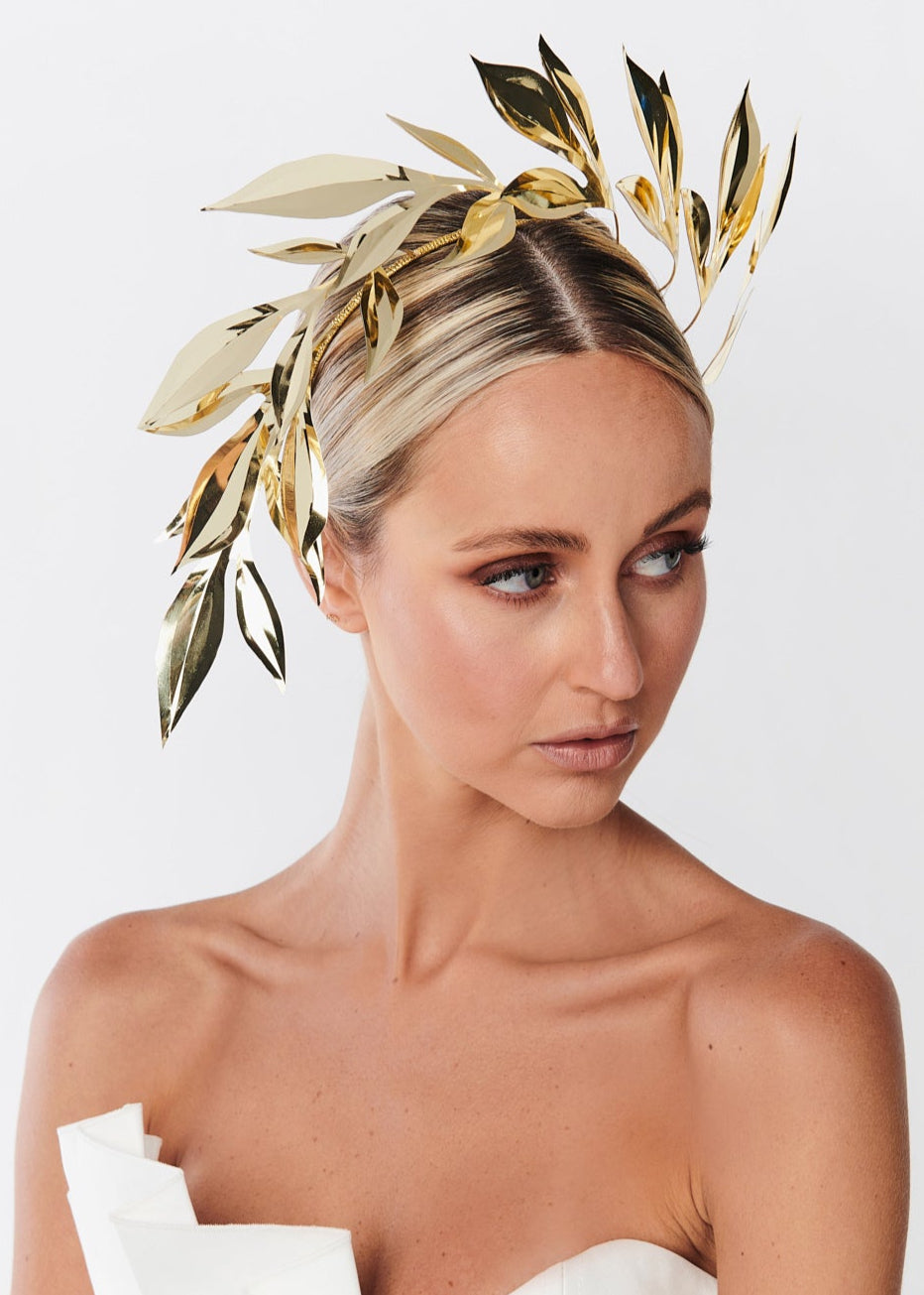 Woman wearing a gold leaf headpiece against a white background
