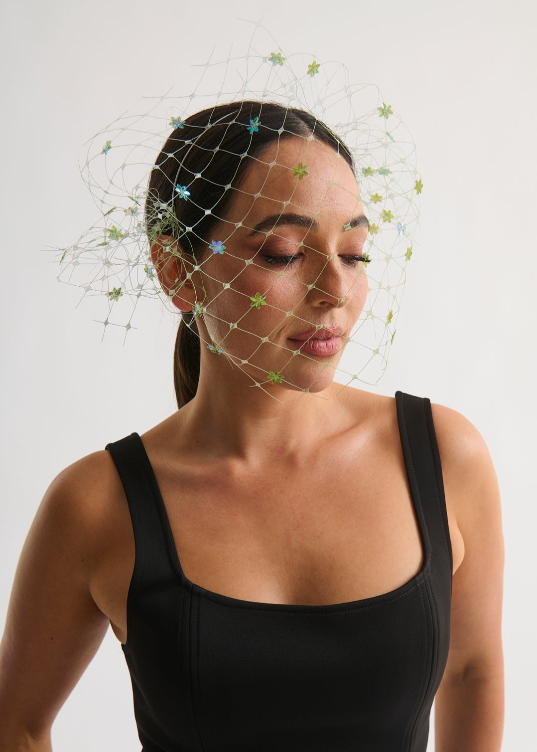 Woman wearing a black dress with a decorative veil headpiece against a white background